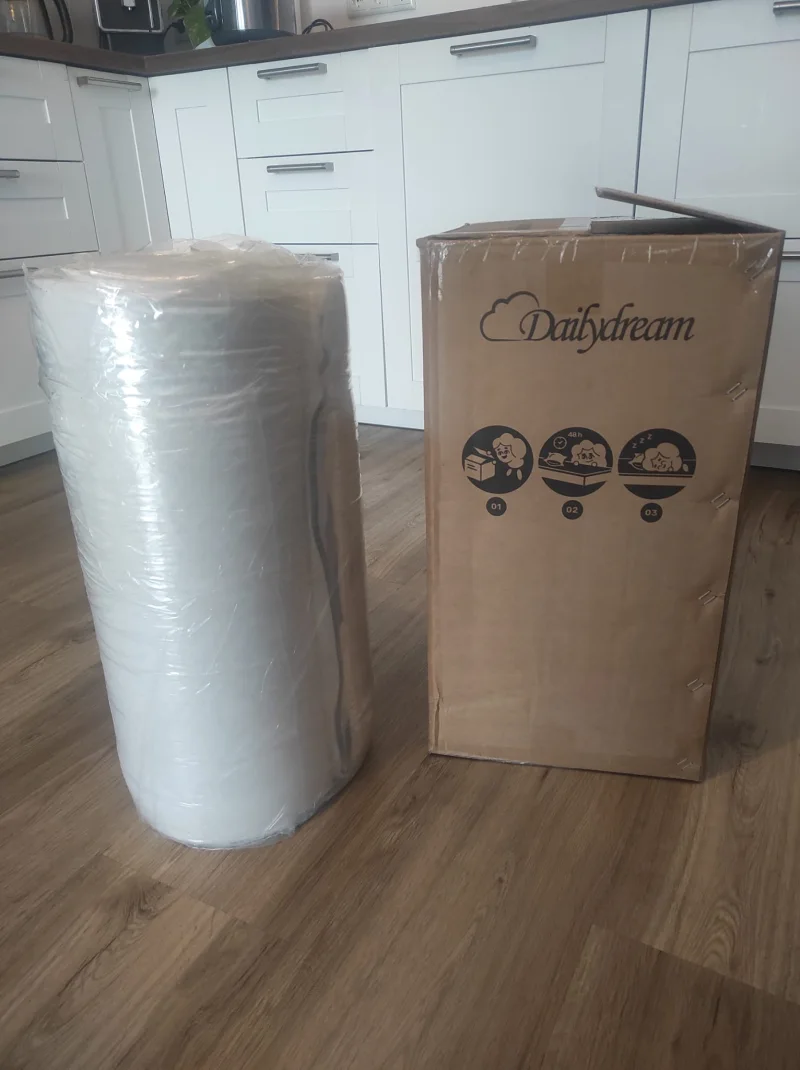 Der gerollte Dailydream Pure Topper neben seinem Versandkarton beim Auspacken