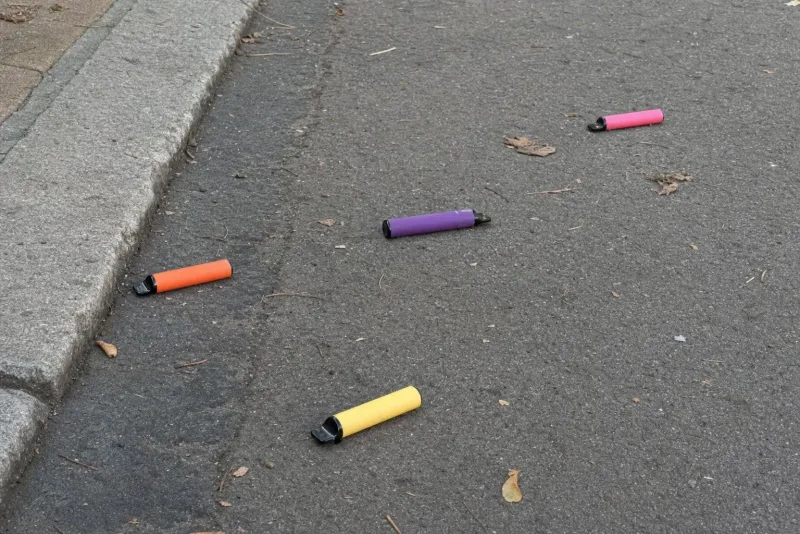Weggeworfene bunte Einweg-E-Zigaretten liegen achtlos auf einem Gehweg am Straßenrand