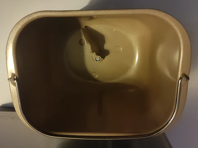 Leere, beige-braun beschichtete Backform des Fornello Supremo mit Bügelgriff und eingesetztem Knethaken, von oben fotografiert