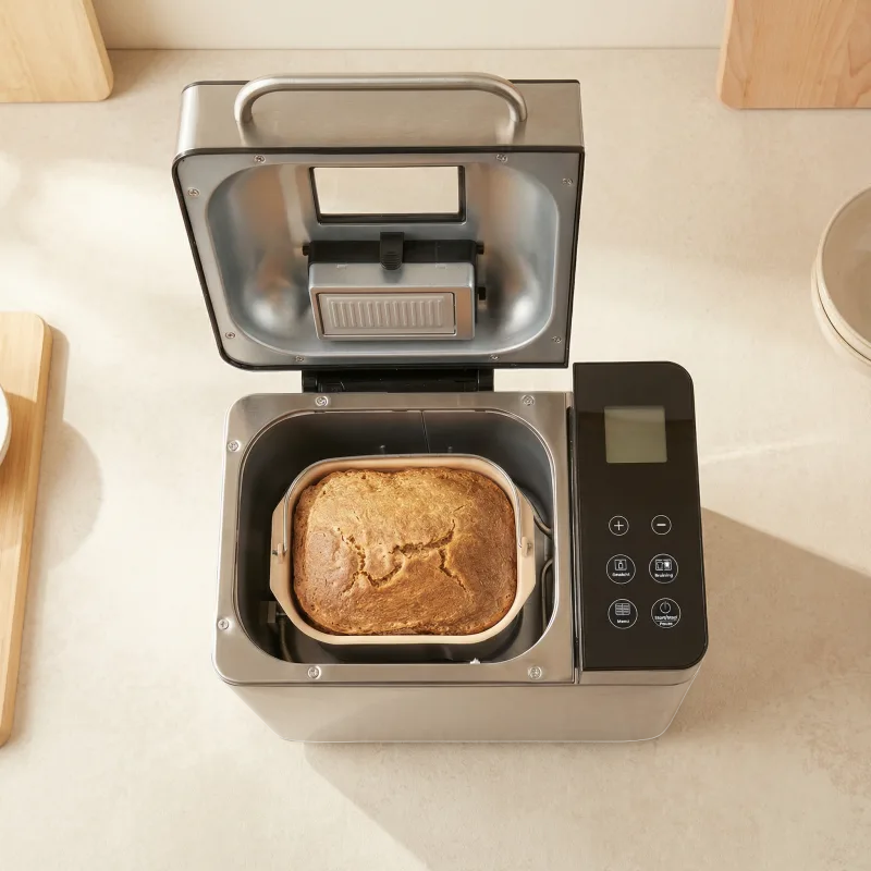 Fornello Supremo von oben mit geöffnetem Deckel, fertig gebackenes Brot in der beige beschichteten Backform, daneben Display und Sensortasten