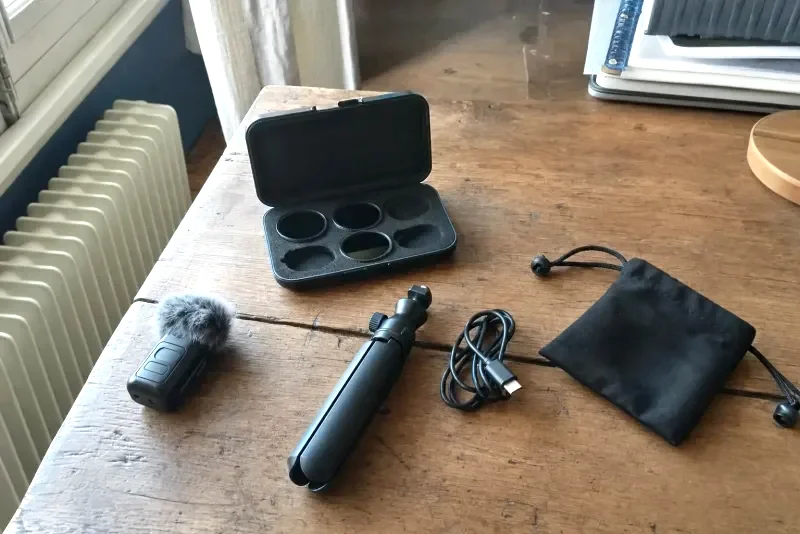 Zubehör einer Pocket-Gimbal-Kamera auf einem Holztisch: Funkmikrofon-Sender mit Windschutz, ND-Filter-Set, Mini-Stativ, USB-C-Kabel und Tasche