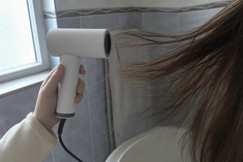 Eine Hand richtet einen High-Speed-Föhn auf langes Haar, das der Luftstrom sichtbar bewegt