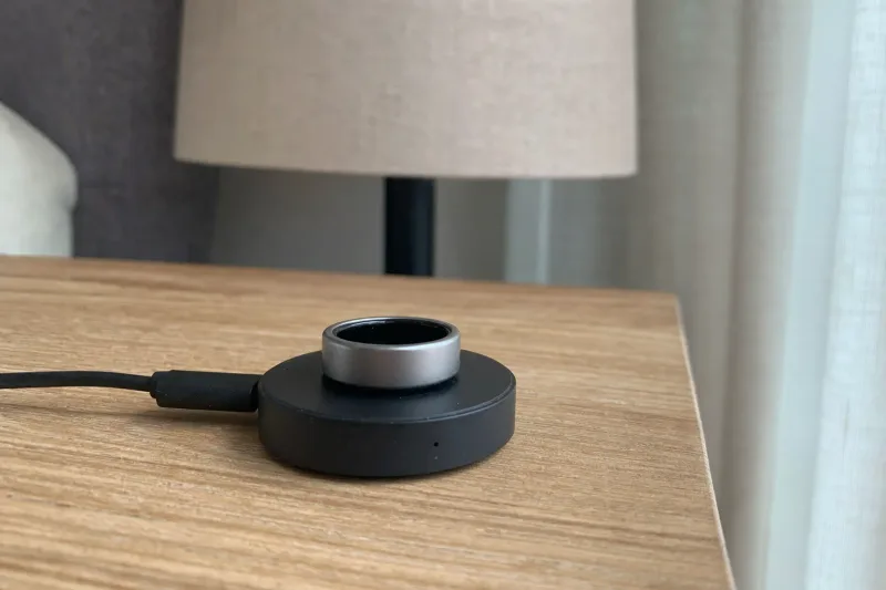 Smart Ring in einer offenen runden Ladeschale auf einem hölzernen Nachttisch bei weichem Morgenlicht