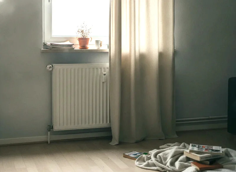 Heizkörper unter einem Fenster, an einer Seite teilweise von einem langen Vorhang verdeckt