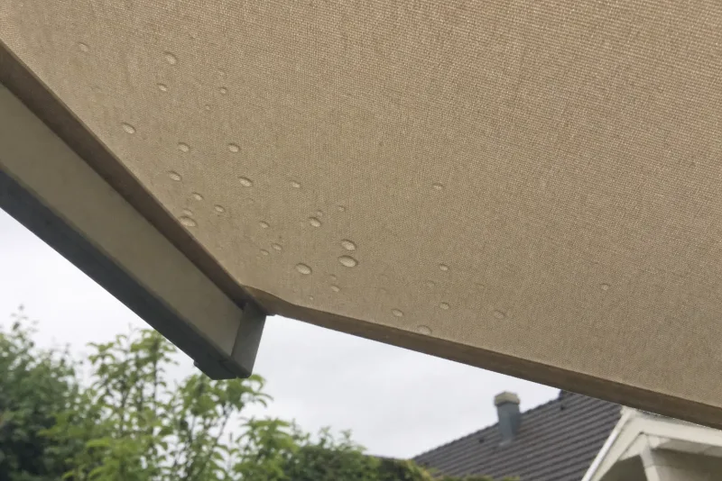 Wassertropfen perlen auf der straff gespannten Bespannung eines Sonnenschirms ab - Hinweis auf eine wasserabweisende Imprägnierung