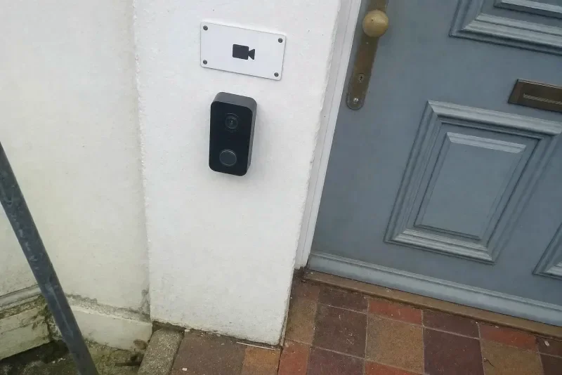 Video-Türklingel neben einer Haustür mit kleinem Kamera-Hinweisschild am Türrahmen