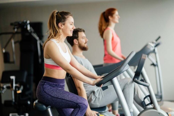 People traning in gym on various machines Menschen trainieren auf Heimtrainer, Crosstrainer und Rudergerät