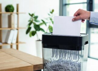 Ein Mann schreddert ein Blatt Papier mit einem Aktenvernichter in einem Büro.