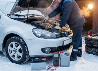 Auto vor Frost-Pannen schützen: Der komplette Wintercheck-Ratgeber Ein Mechaniker repariert ein schneebedecktes Auto mit geöffneter Motorhaube im Freien.