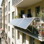 Balkonkraftwerk Ertrag: Die Wahrheit über kWh, Kosten und Amortisation Außen am Geländer eines bepflanzten Balkons montierte Solarpaneele über einer belebten Stadtstraße.