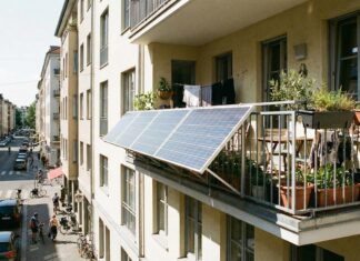 Außen am Geländer eines bepflanzten Balkons montierte Solarpaneele über einer belebten Stadtstraße.