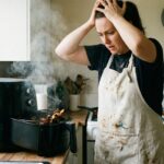 Die 10 häufigsten Fehler im Umgang mit einer Heißluftfritteuse Eine Frau in der Küche blickt besorgt auf eine rauchende Heißluftfritteuse.