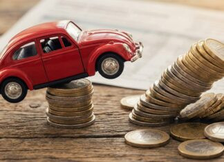Kfz-Versicherung 2026: Die versteckten Schadenfreiheits-Killer der Billig-Tarife Roter Spielzeug-Käfer steht auf einem Stapel Euromünzen, daneben ein umfallender Münzturm auf Holzgrund.