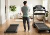 Ein Mann vergleicht im Wohnzimmer ein flaches Walking Pad mit einem großen, klassischen Laufband.