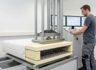 Ein Mann bedient eine Maschine, die Druck auf einen Matratzen-Querschnitt mit Federkern ausübt.