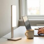 Tageslichtlampen im Test-Check 12/2025: Endlich Schluss mit Winterdepression? Schreibtisch mit Laptop, Tasse und Tageslichtlampe. Eine Person tippt.